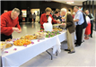 People stand along buffet tables plating food.