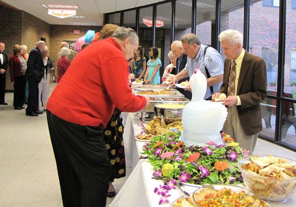 People walk down buffet tables plating food.